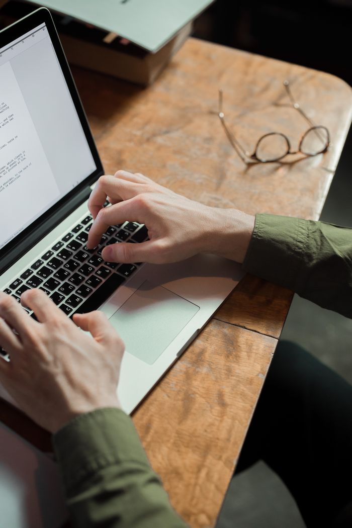 Close-up of hands typing on a laptop, set against a wooden desk with a pair of glasses.